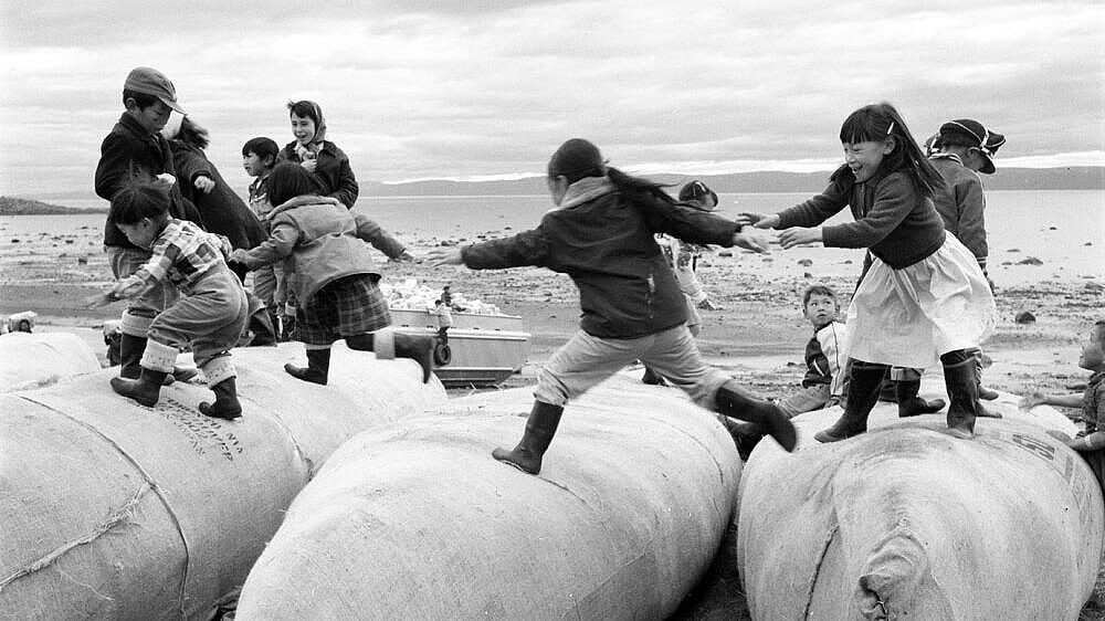 Mehrere Kinder springen auf umgedrehten Kanus an der Küste entlang.