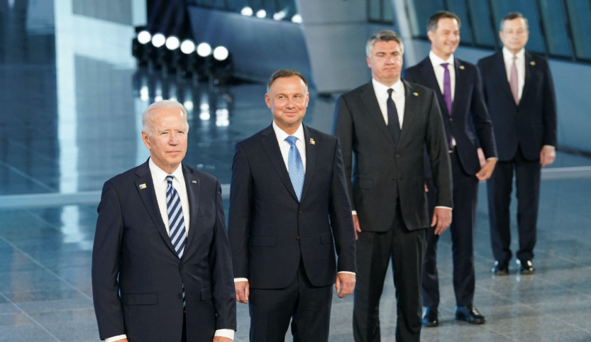 Fünf Männer in dunklem Anzug und weißem Hemd stehen mit hängenden Armen diagonal hintereinander. Sie lächeln und schauen links an der Kamera vorbei.