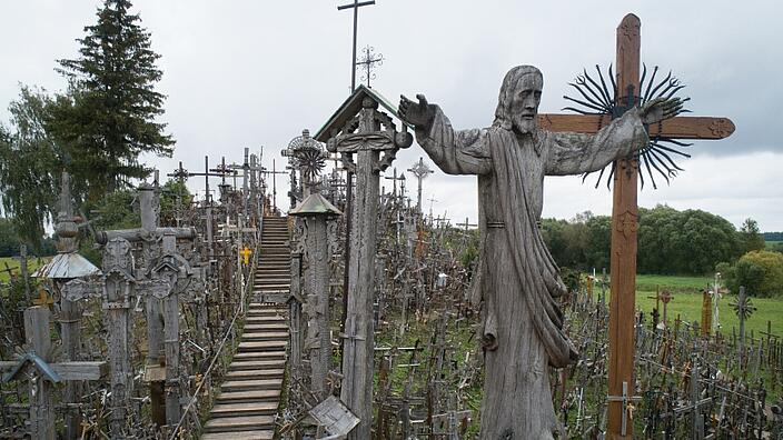 A staircase amidst many crosses made of wood and metal leads up the hill. In the center of the picture is a large statue of Christ.