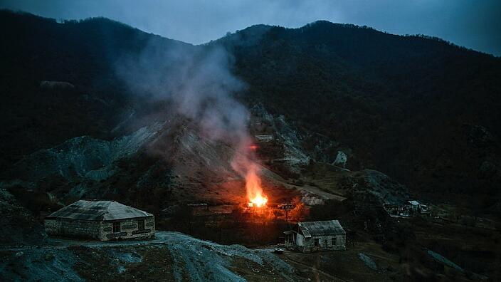 Es ist Nacht. In den Bergen in der Region Bergkarabach stehen vereinzelt Steinhäuser. Ein großes Feuer erhellt die nähere Umgebung.