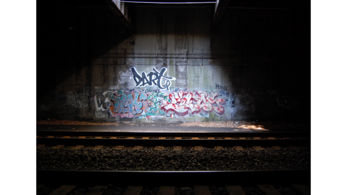 A dark room with a graffiti wall, which is illuminated by a light. A track runs in front of it.