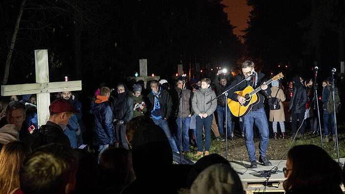 Menschenversammlung mit Holzkreuzen im Hintergrund, ein Mann spielt Gitarre