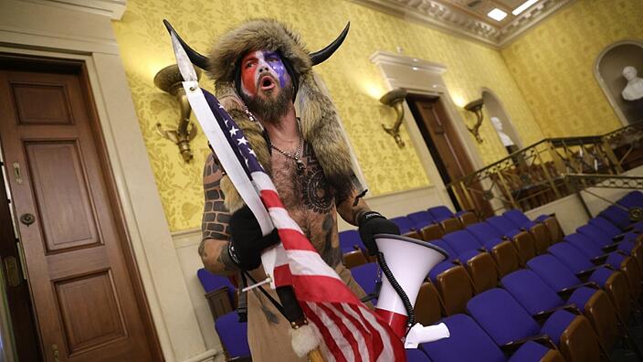 A protester wears a fur hat with buffalo horns and holds the American flag during the storming of the U.S. Capitol on Jan. 6, 2021, in Washington, D.C.