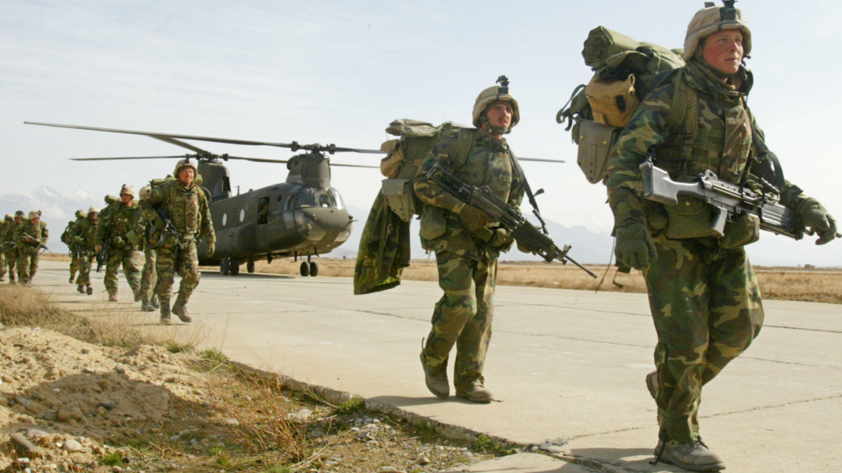 Eine Truppe voll ausgerüsteter US-Soldaten laufen entlang eines Rollfeldes. Im Hintergrund steht der Militärhubschrauber.