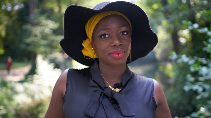 Porträt: Maimouna Coulibaly schaut in die Kamera, sie trägt einen Hut mit breiter Krempe und Lippenstift 