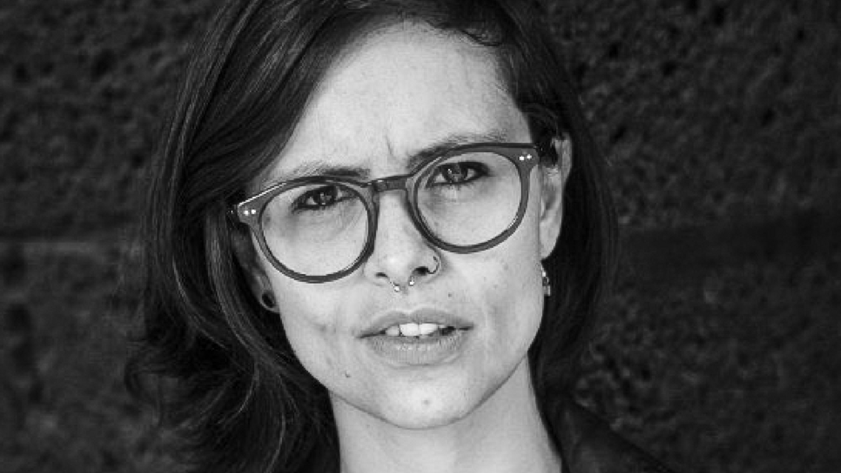 Ein schwarz weiß Porträtfoto von der Politikerin Lucia Riojas Martinez. Sie hat halblange dunkle Haare und trägt eine Brille.