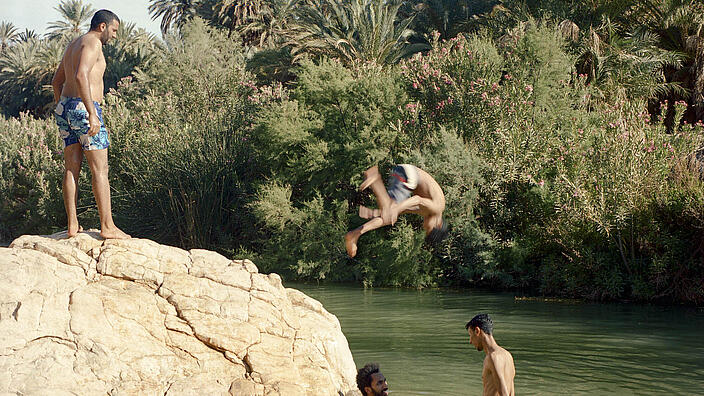 Einige junge Männer baden in einem Teich, umgeben von einem Felsen und dichtem Gebüsch 