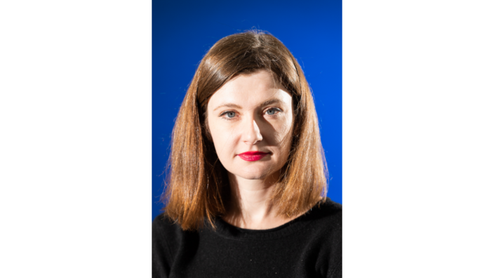 A portrait of the writer Olga Gryaznova against a blue background. She has half-length straight hair and is looking into the camera.