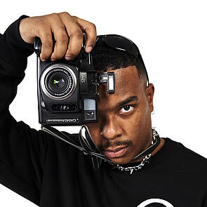 Young man looks into the camera, he also holds a camera in front of his eye