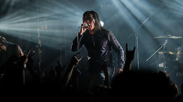 Der Metal-Star Freddy Lim steht während eines seiner Konzerte auf der Bühne. Er hat ein Mikrofon in der Hand und singt. Es ist dunkel, der Sänger ist dunkel gekleidet, er hat lange glatte dunkle Haare. Arme seiner Fans in der ersten Reihe strecken sich ihm entgegen. 