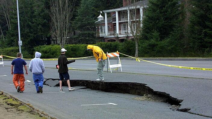 Four people are standing on a road whose asphalt slab is broken in the middle and shifted.
