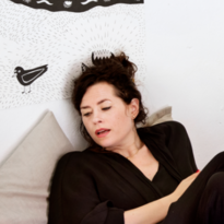Die Comiczeichnerin Liv Strömquist liegt mit dem Rücken an die Wand gelehnt und überschlagenen Beinen in ihrem Bett. 