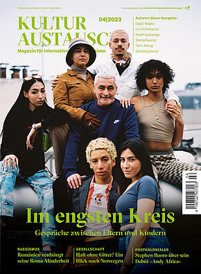 Das Cover der Ausgabe IV/2023 von KULTURAUSTAUSCH. Auf dem Foto ist eine Gruppe Menschen zu sehen, die sich offenbar nahe stehen. Im Zentrum ein etwas älterer Mann mit kurzen grauen Haaren, um ihn herum gruppiert sechs junge Menschen. 