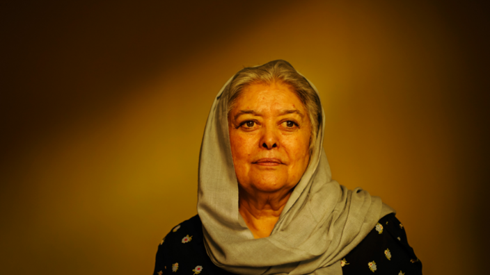 A portrait of an elderly woman. Gray hair comes out from under the light green headscarf. She looks past the camera on the left.