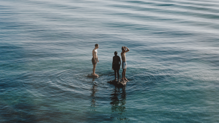 Drei Menschen stehen auf einer Wasserfläche. 