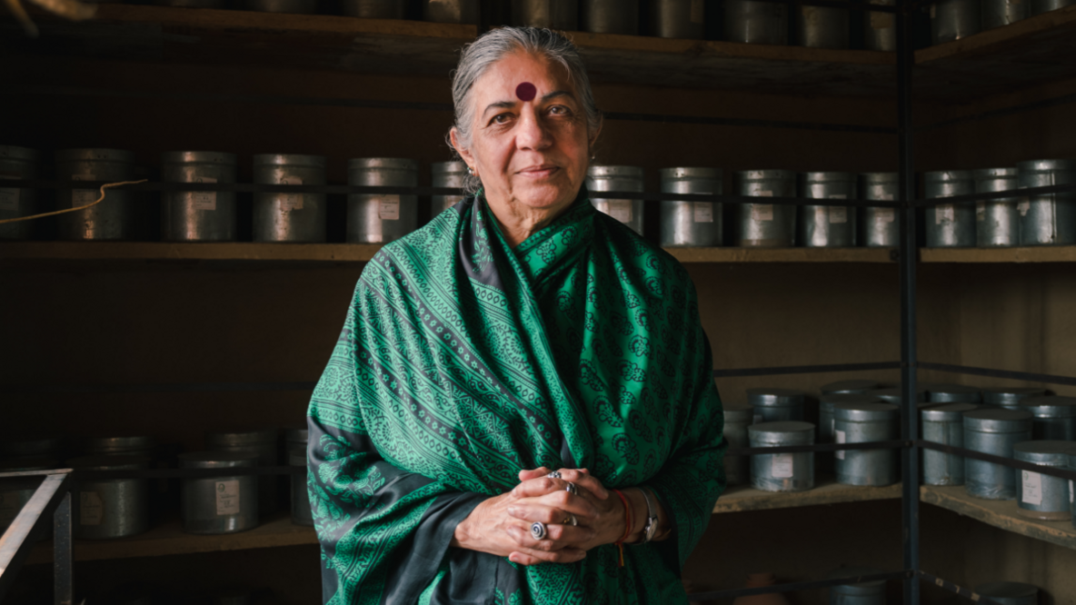 Vandana Shiva schaut mit gefalteten Händen im grünen Sari freundlich in die Kamera