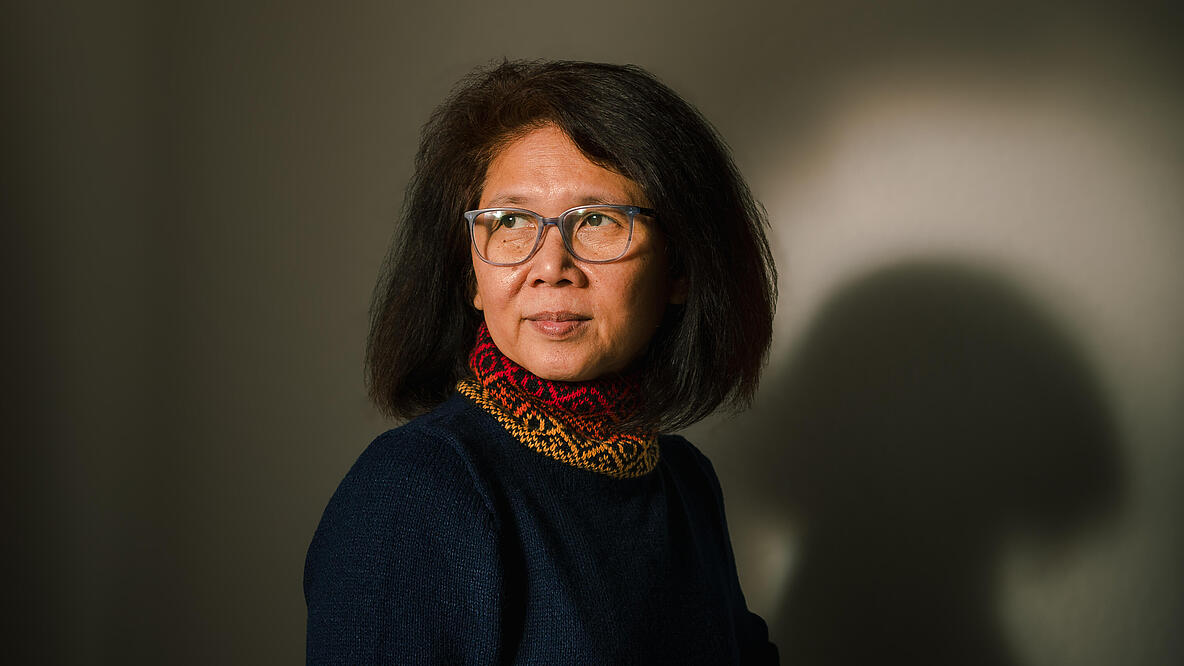  A portrait of Ma Thieda, aged around 55. Her hair is chin-length, she is wearing a dark sweater and glasses and is looking past the camera on the right.