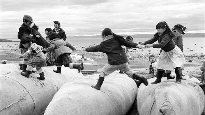 Mehrere Kinder springen auf umgedrehten Kanus an der Küste entlang.