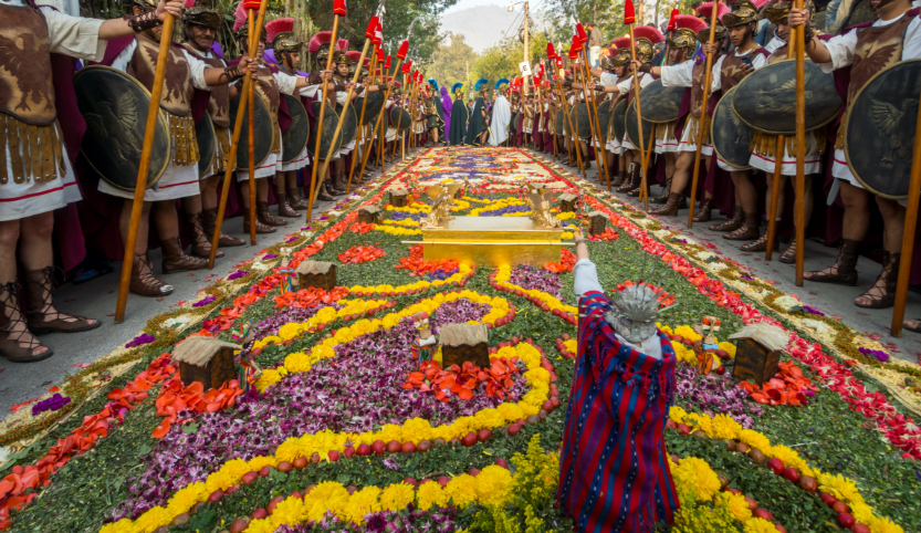 Am Rande eines großen bunten Blumenteppichs stehen Männer in historischem Gewand mit Speer und Schild.  