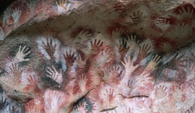 On a gray, white, red cave wall are many different hands.