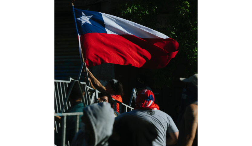 A Chilean man holds the Chilean flag. Other people are standing next to him.